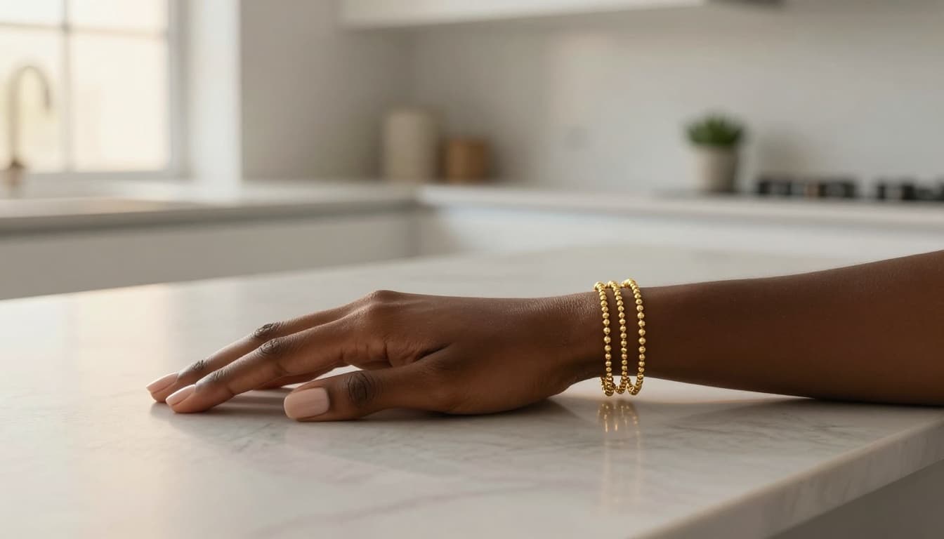 Simple stack of 14k gold bead bracelets worn on a wrist against a marble surface