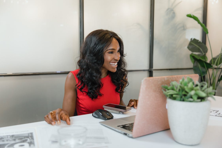 Woman smiling while working on a laptop at a desk in a modern office