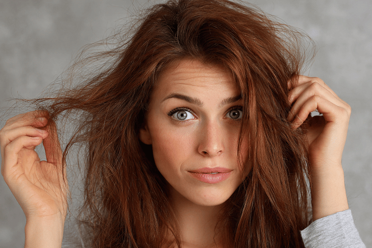 Woman holding frizzy hair strands, showing common signs of dry, frizzy hair