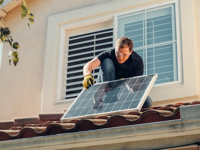 Solar panel installer placing a solar panel on a residential rooftop during installation