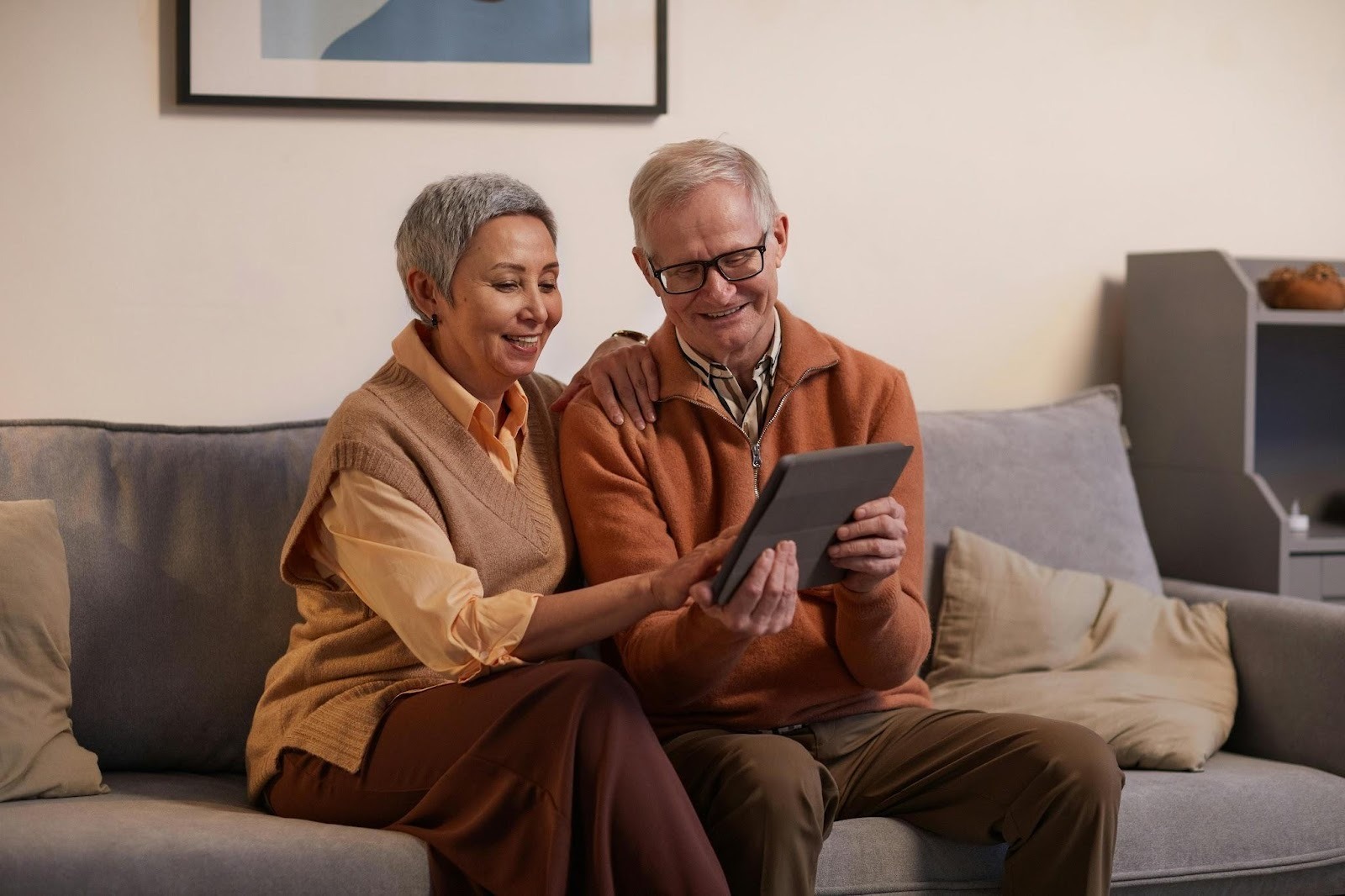 Senior couple sitting on couch reviewing finances on tablet