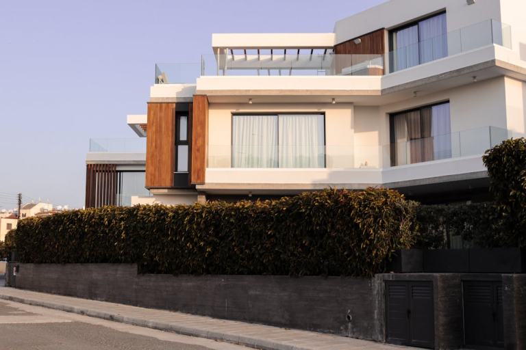 Modern two-story home exterior with balcony, large windows, and landscaped hedge