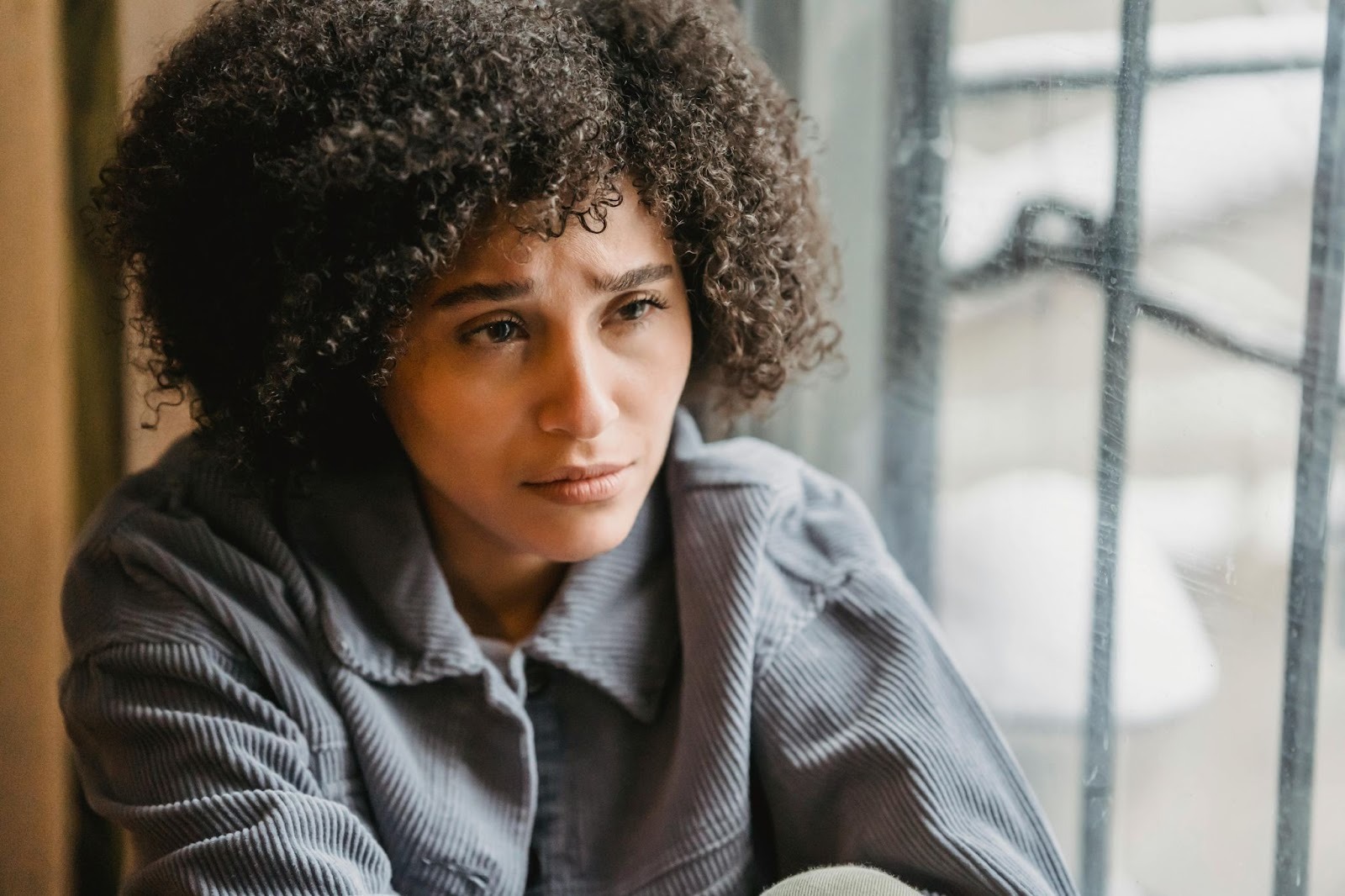 Person sitting by a window looking thoughtful, representing the emotional challenges of addiction and recovery