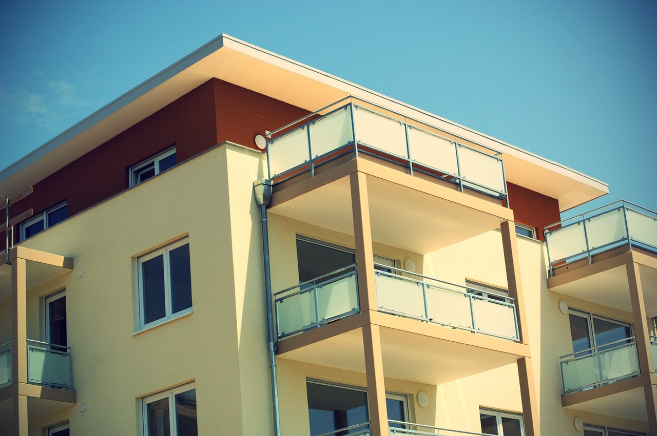 Modern apartment building with balconies and glass railings under a blue sky
