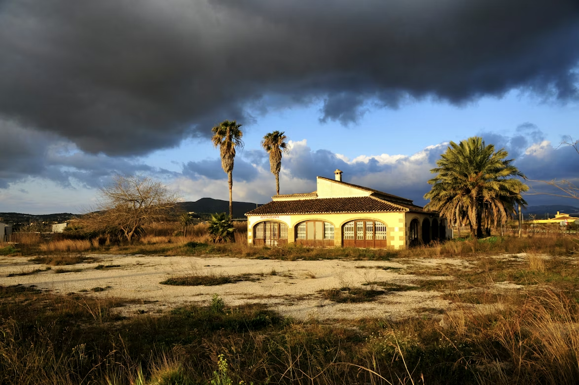 Single-story home under dark storm clouds with palm trees nearby