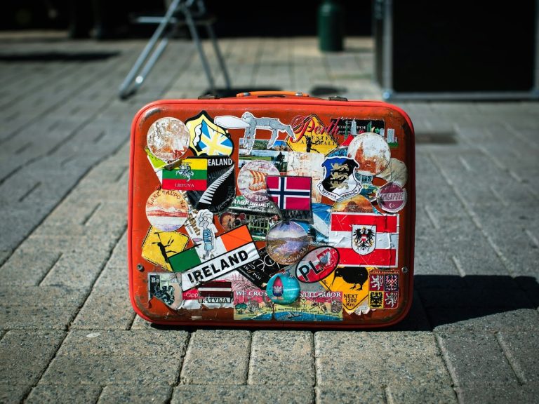 Red vintage suitcase covered in travel stickers sitting on a paved walkway before a trip
