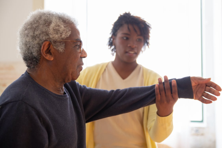 Caregiver helping an elderly man with arm exercises during in-home senior care session