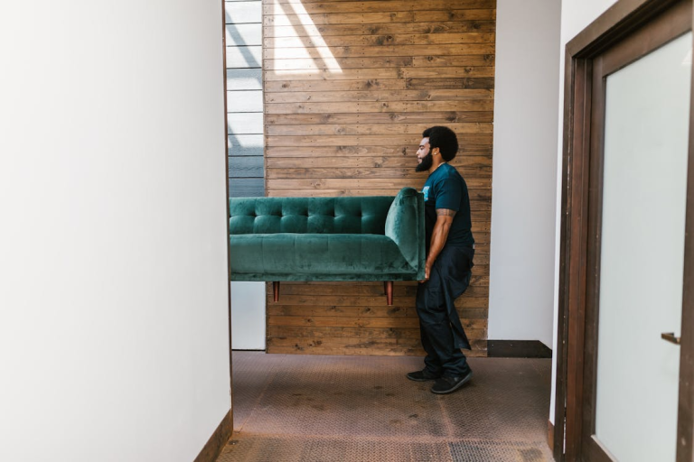 Mover carrying a green sofa through a hallway while relocating to a new home