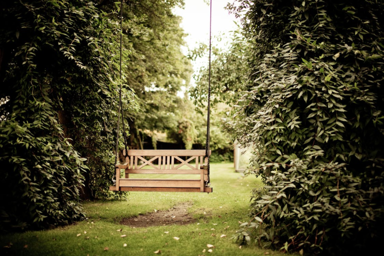 Wooden garden swing in a lush green backyard ready for summer