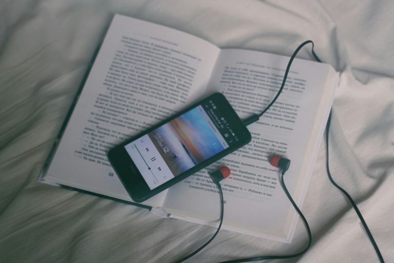 Smartphone playing music resting on an open book with earphones, representing simple hobbies during busy life