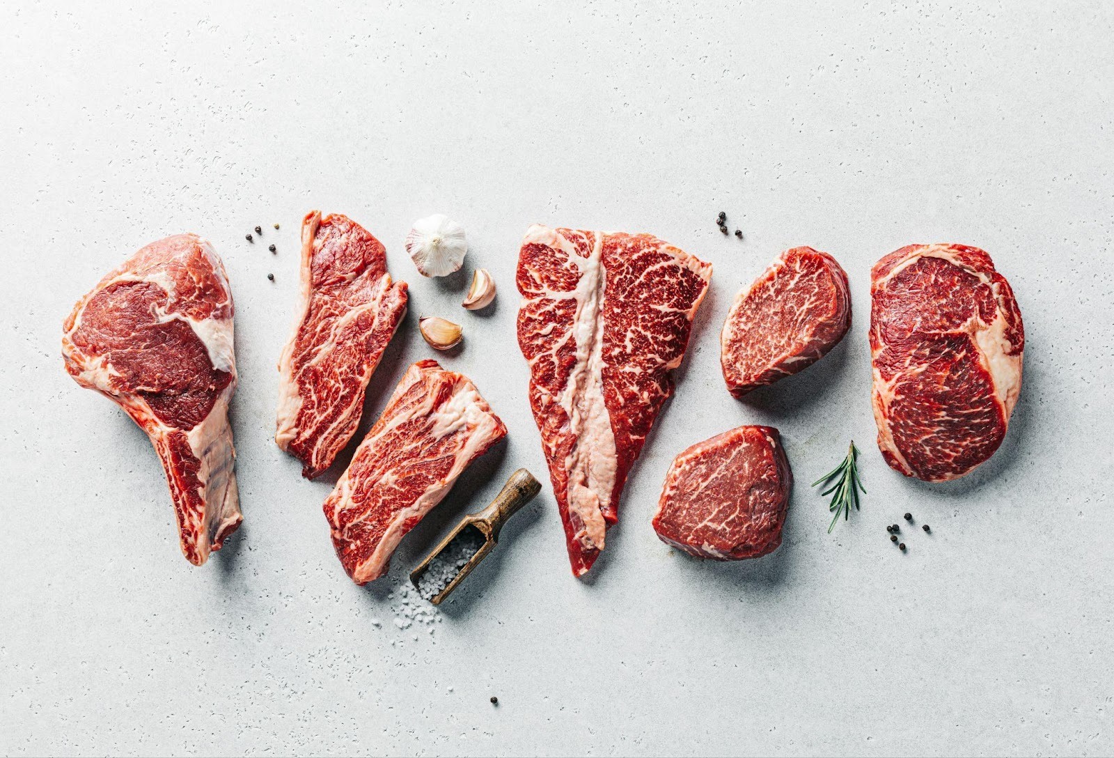 Various cuts of raw red meat arranged on a light surface