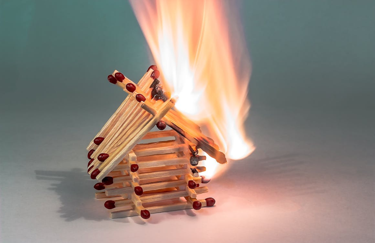 Small house made of matchsticks burning with flames on a white background