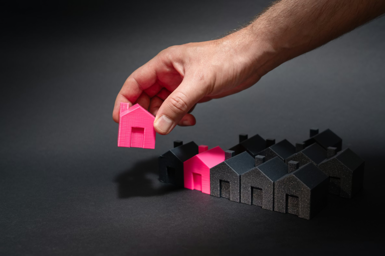 Hand placing a house model among other small houses representing rental property investment