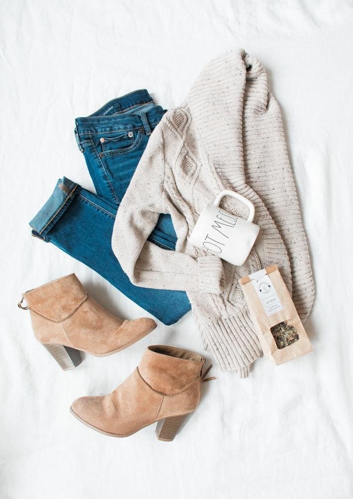 Flat lay of a casual outfit with blue jeans, cream sweater, ankle boots, and accessories showing a simple personal style