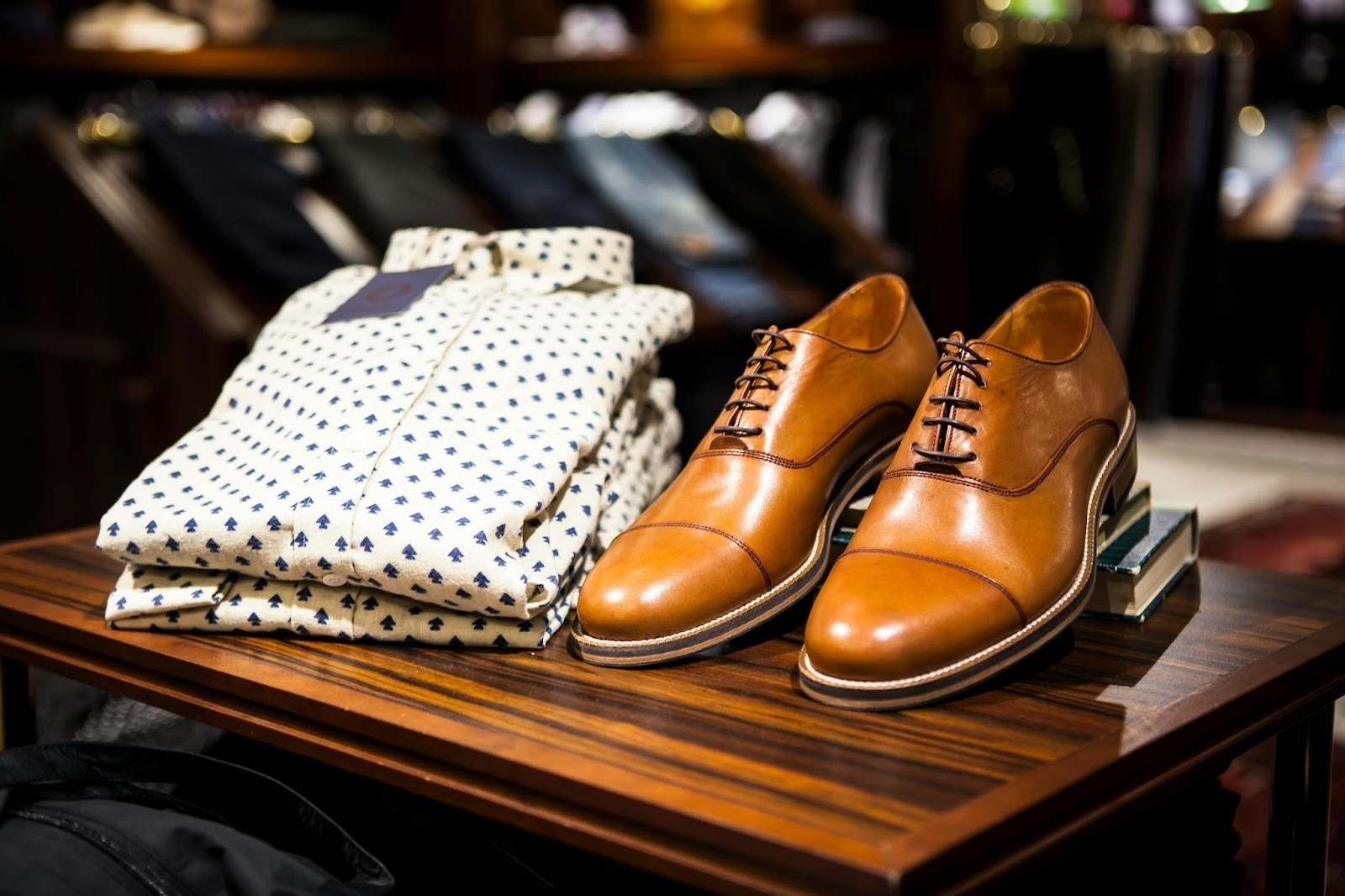 Brown leather dress shoes next to a folded patterned shirt on a boutique display table