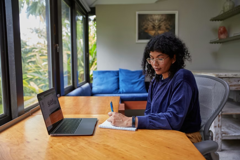 woman working on laptop and writing notes while planning ways to diversify income streams