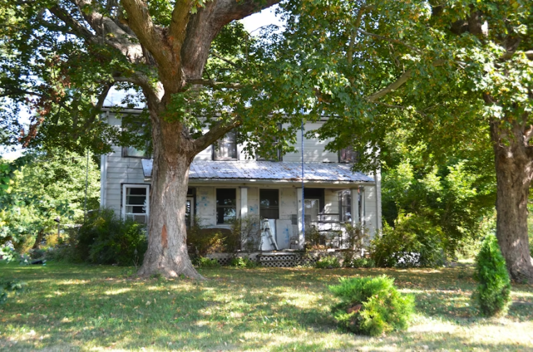 older home surrounded by large trees representing rebuilding and restoring a home after damage