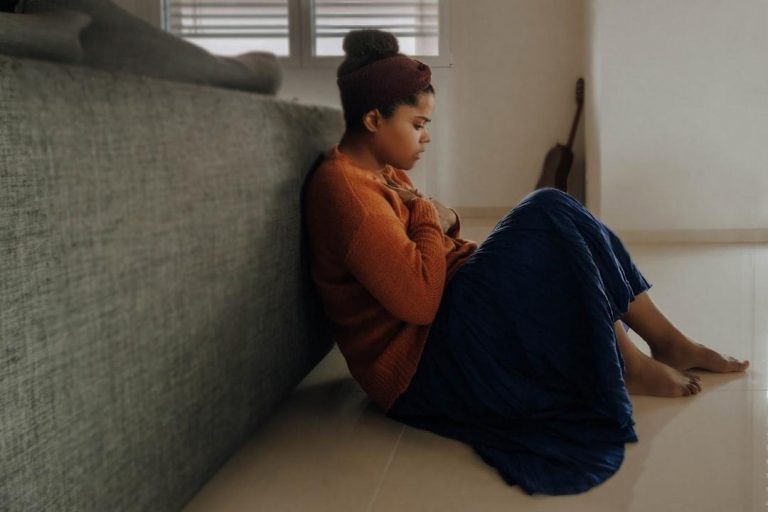 woman sitting alone on the floor looking overwhelmed and deep in thought