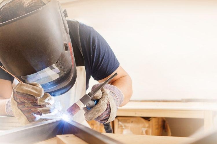 Male in face mask welds with argon-arc welding