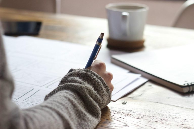 Person writing notes at a desk with notebook and coffee to improve learning efficiency