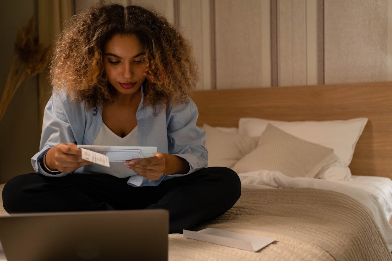 Woman sitting on bed reviewing utility bills and expenses at home