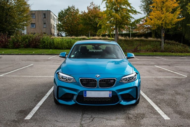 blue car parked in an empty parking lot with trees in the background during fall