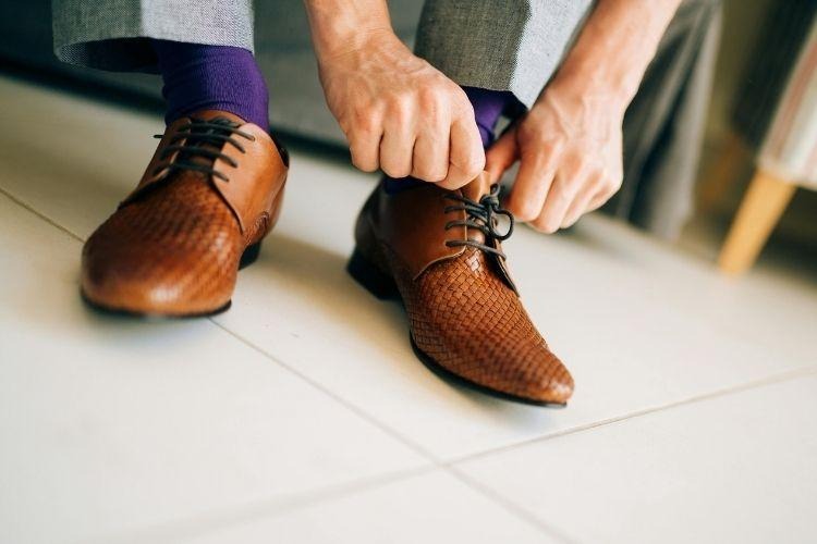 Man tying brown leather shoes in stylish socks