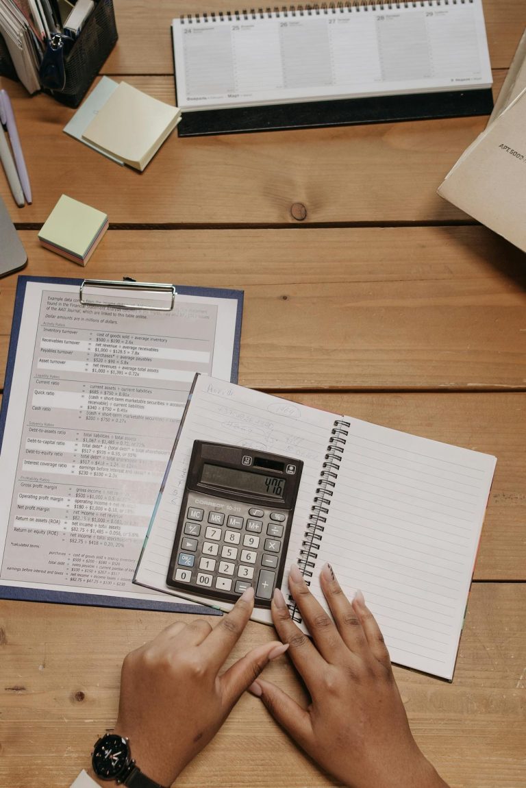 Hands using a calculator with payroll forms and a notebook on a desk for small business payroll planning.