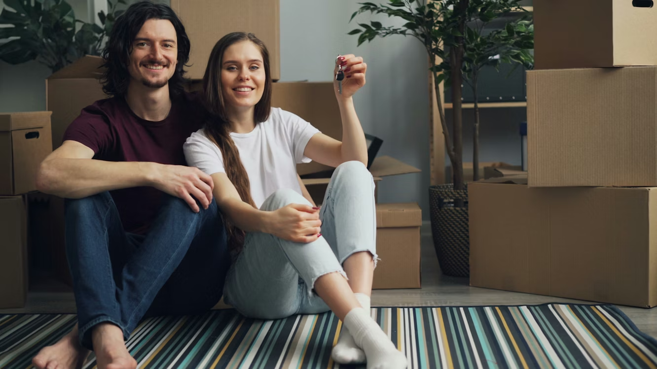Couple holding house keys while sitting among moving boxes in a new property.