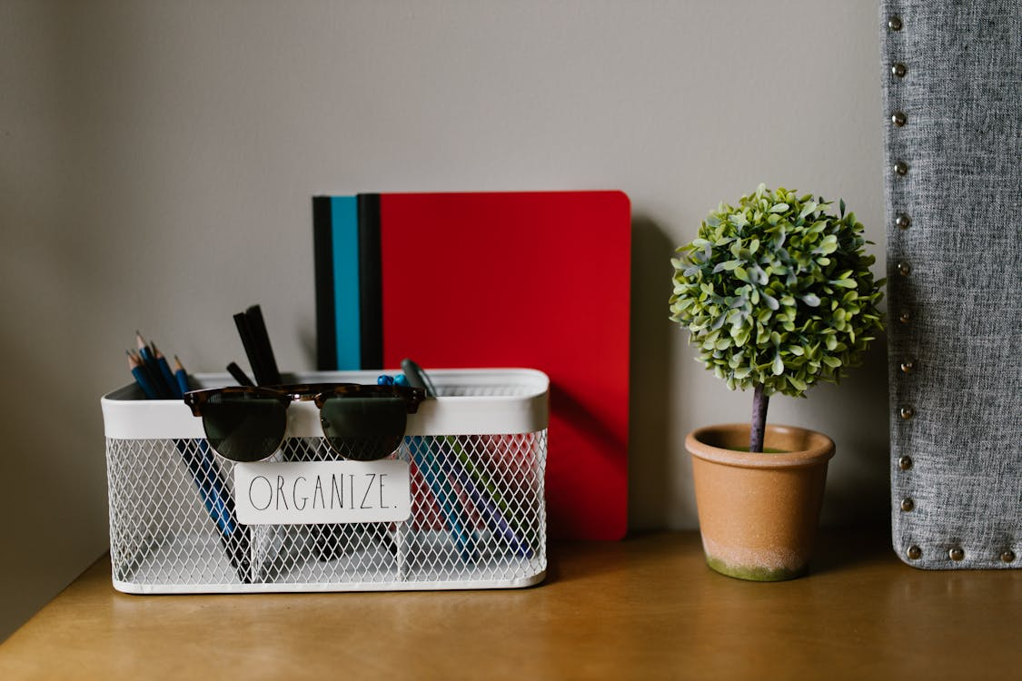 Organized desk with office supplies, notebooks, and storage containers arranged neatly on a shelf