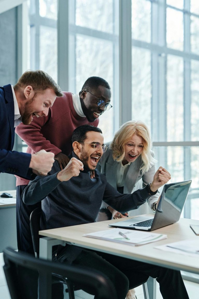 Business team celebrating together at a laptop while working in a modern office.