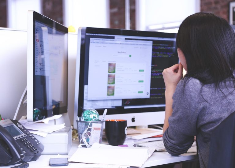 Employee sitting at a desk surrounded by multiple screens and workplace notifications.