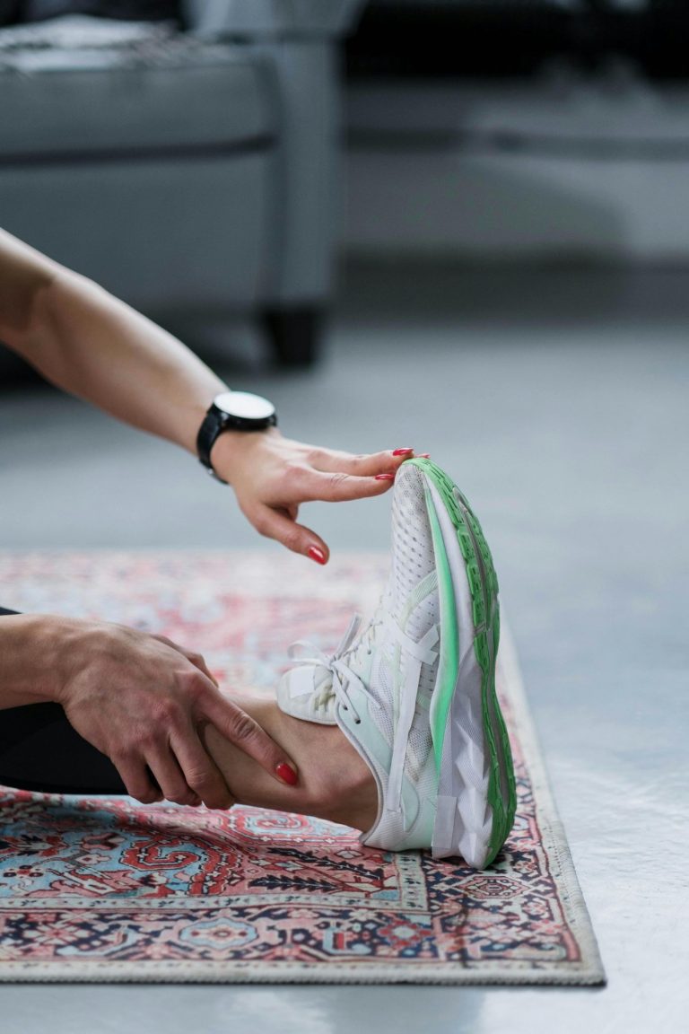 Person stretching their leg on a rug while wearing athletic shoes indoors.