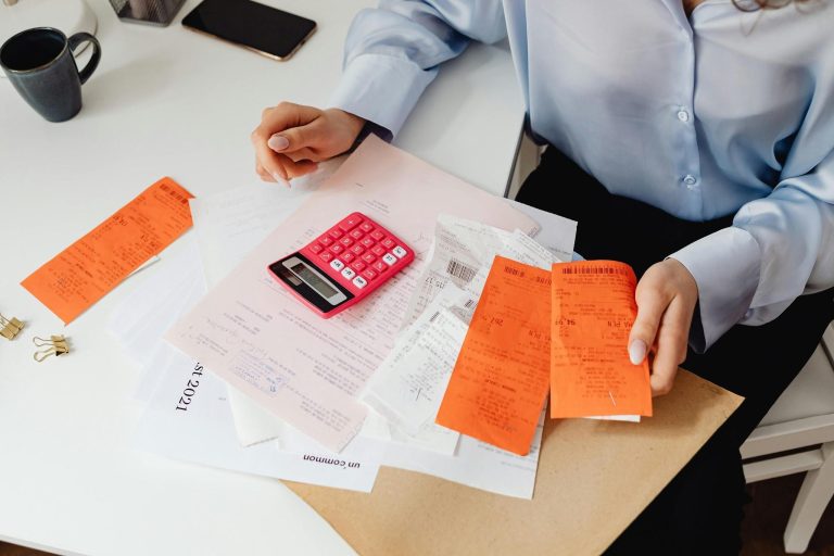 A woman reviews receipts and calculates expenses at a desk with a calculator.