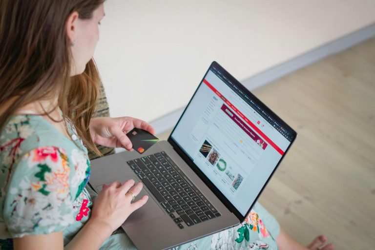 Woman shopping online on a laptop while holding a credit card for an ecommerce purchase.