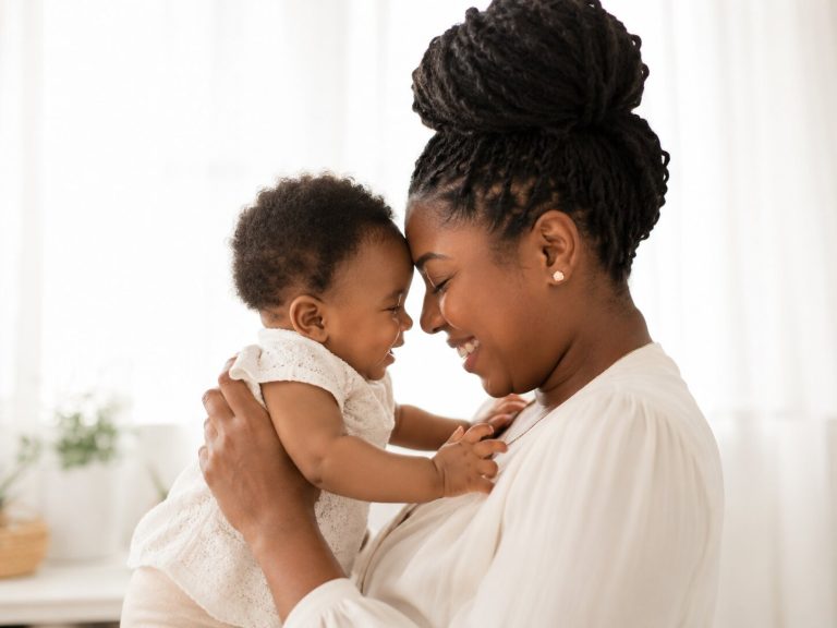 Black mother holding her baby in a bright home setting during a quiet moment of connection and care.