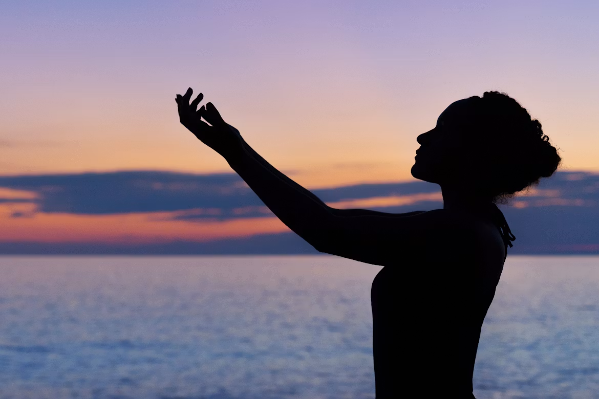 Silhouette of a woman practicing mindful movement by the water at sunset