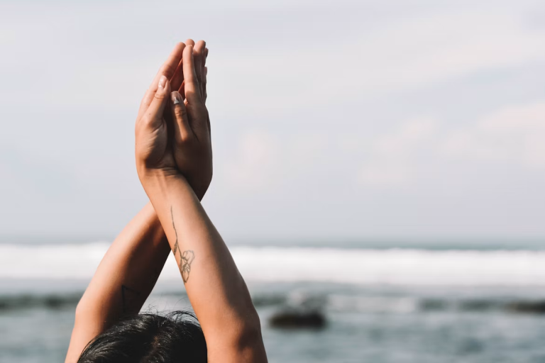 Person raising hands in a grounding and mindfulness exercise near the ocean
