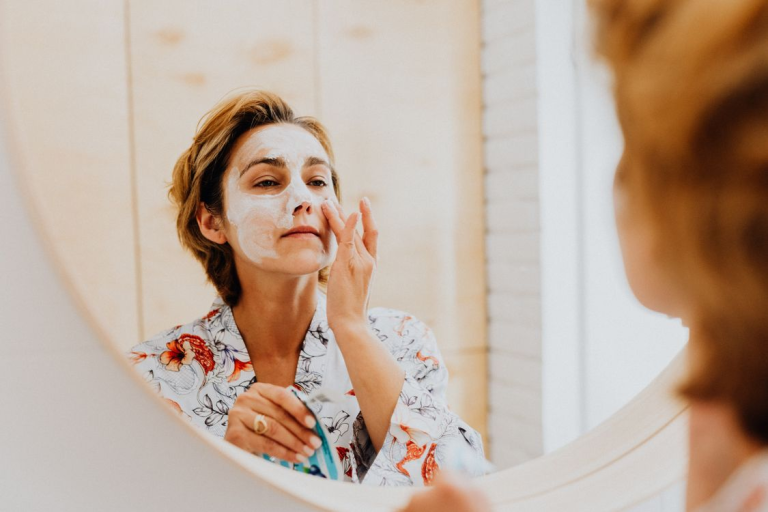Woman applying a facial skincare treatment while looking in a mirror as part of a healthy aging self-care routine.