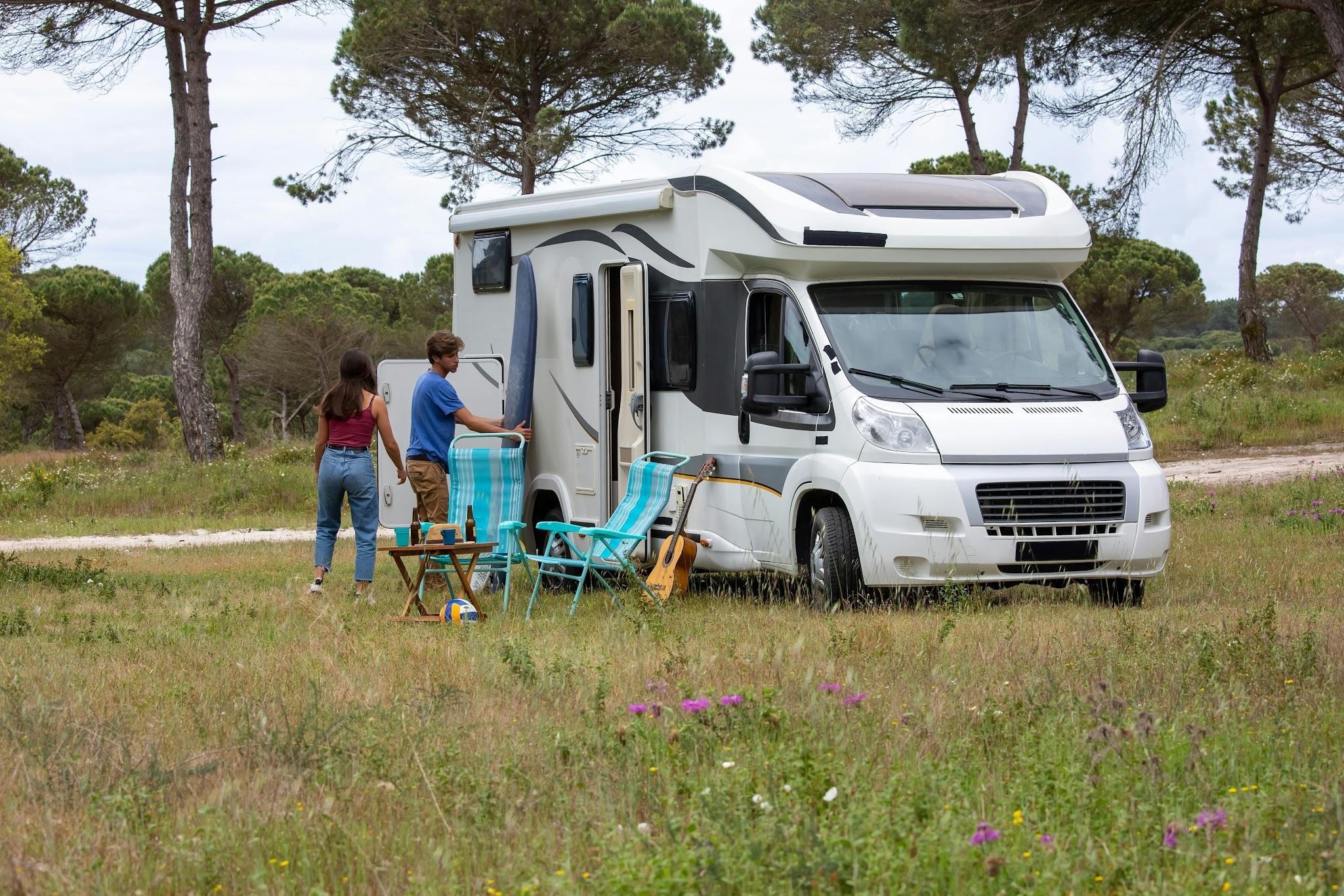 Travelers setting up outdoor chairs and relaxing space beside their RV at a campsite.