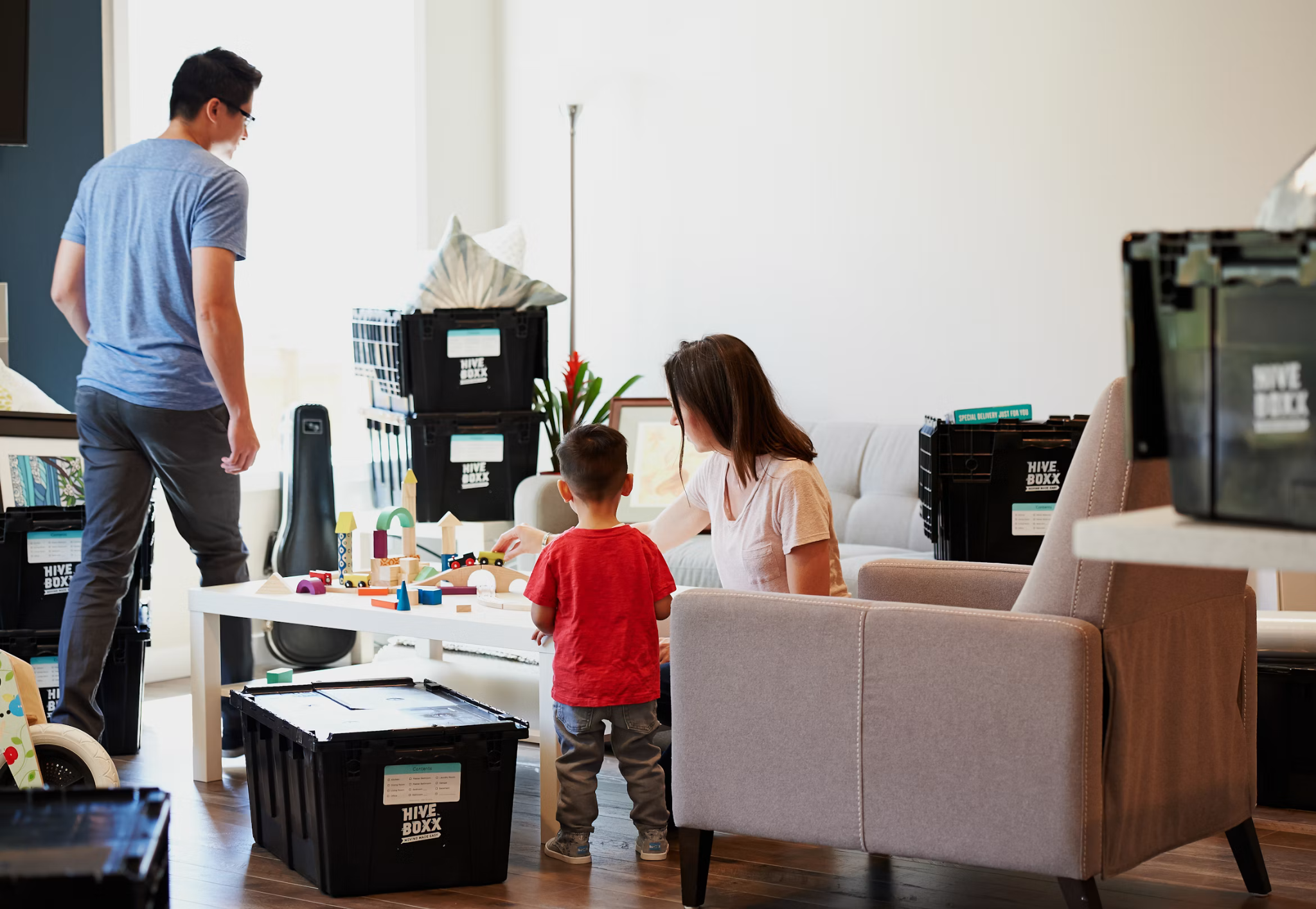 Family settling into a new home with moving boxes while a child plays in the living room during the moving process