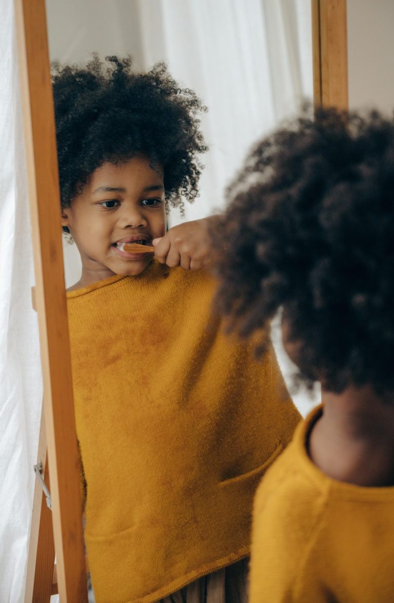 Young child brushing their teeth while looking in a mirror as part of a daily oral hygiene routine.