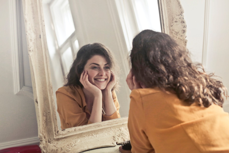 Woman smiling at her reflection in a mirror while practicing positive self-talk