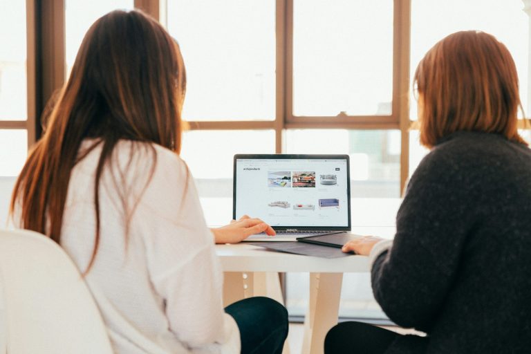Two business owners reviewing a company website on a laptop while discussing improvements to user experience and design.