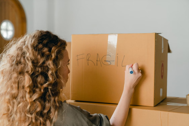 Woman labeling a moving box marked fragile while preparing for a household move