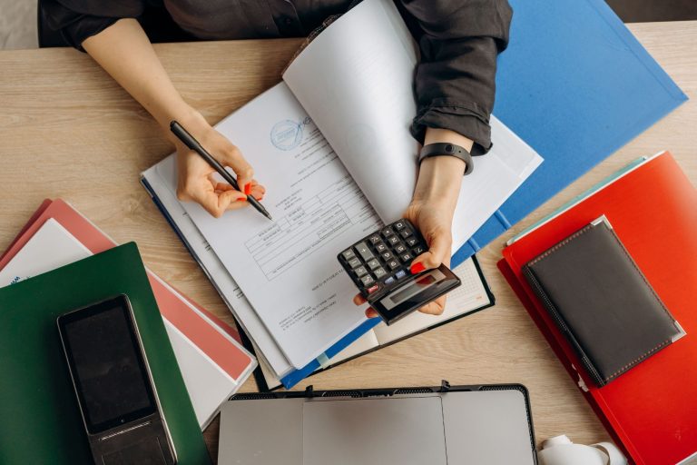 Business owner reviewing financial documents and using a calculator to track expenses and manage business costs.