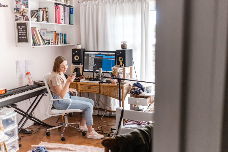 Content creator recording audio in a home studio with a microphone, computer, speakers, and recording software for podcast and audio content creation.