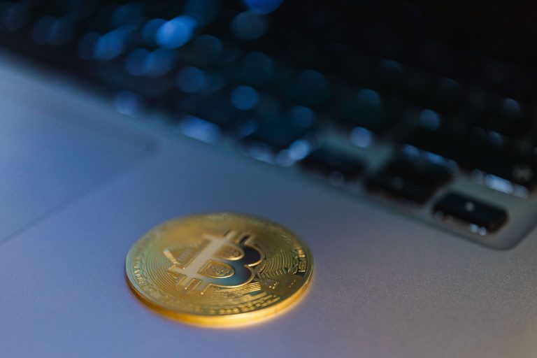 Bitcoin cryptocurrency coin placed beside a laptop computer representing digital investments and crypto tax reporting