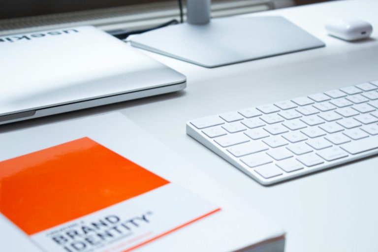 Modern workspace with branding materials, computer accessories, and a brand identity guide used for business marketing planning.