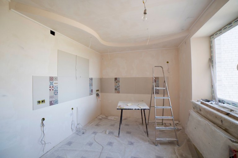 Empty room prepared for a home renovation with floors covered, a ladder, and construction materials ready for remodeling.